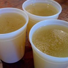 three plastic cups filled with liquid sitting on top of a wooden table