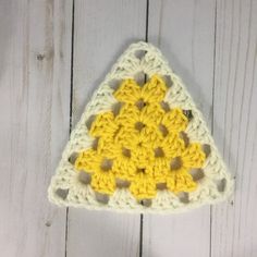 a crocheted triangle with yellow and white squares on it sitting on a wooden surface