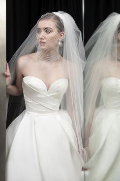 a woman wearing a wedding dress and veil in front of a mirror with her reflection