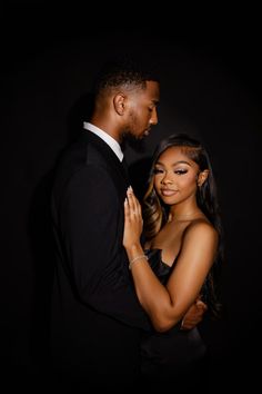 a man and woman standing next to each other in front of a black background with their arms around each other