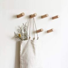 a canvas bag hanging on the wall with wooden pegs attached to it and flowers in front