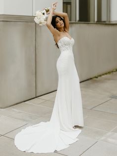 a woman in a white wedding dress posing on the sidewalk with her arms behind her head