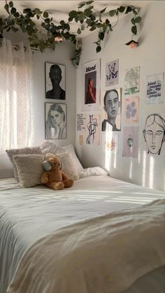 a bed with white sheets and pictures on the wall above it, along with a teddy bear