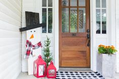 a snowman is standing in front of a door with two lanterns on the porch