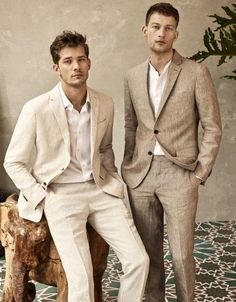 two men in suits standing next to each other on a wooden bench with plants behind them