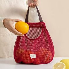 a woman holding an orange and a mesh bag with sheep stickers on the side