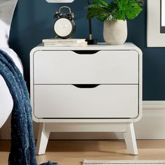 a white nightstand with two drawers and a clock on the side table next to it