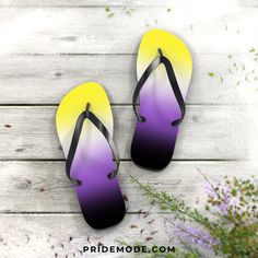 two pairs of flip flops sitting on top of a wooden floor next to flowers