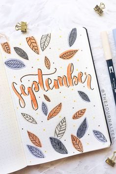 an open notebook with the word november written in orange and blue leaves on it next to a cup of coffee