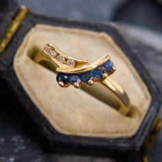 a gold ring with blue and white stones on it sitting in a box next to a pair of scissors