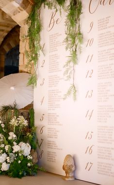 an arrangement of flowers and greenery is displayed next to a wedding seating plan on a wall