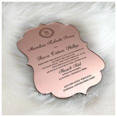 a pink and gold wedding card with an ornate design on the front, sitting on a white furnishing