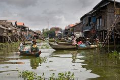 some people are riding in small boats on the water near buildings and trees with green leaves