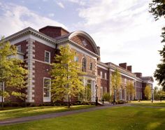 a large brick building sitting on the side of a lush green field next to trees