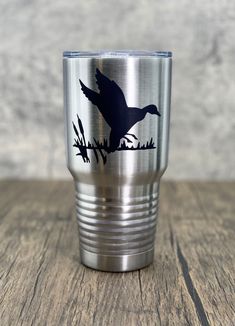 a stainless steel tumbler with a duck silhouette on the side and grass behind it