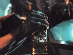 a man holding a bottle of havana club on top of a table in front of other people