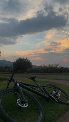 two bikes are parked on the grass in front of some trees and mountains at sunset