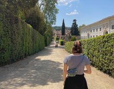 a woman walking down a road next to tall hedges