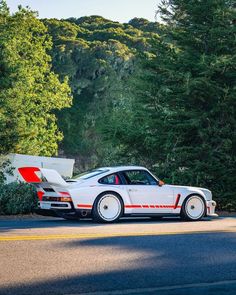 a white sports car parked on the side of the road next to some pine trees