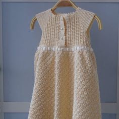 a white knitted dress hanging on a clothes hanger in front of a blue wall