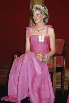 a woman in a pink dress sitting on a chair wearing a tiara and necklace