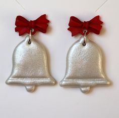 two silver bells with red bows hanging from the side on a white background, one is shaped like a bell and the other is shaped like a bell