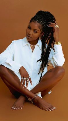 a woman with dreadlocks sitting on the ground in front of a brown background