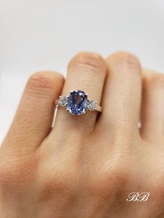 a woman's hand holding an engagement ring with a blue sapphire and diamond accents