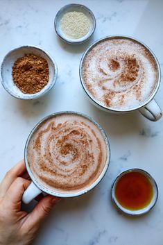 two cups of hot chocolate with cinnamon sprinkles and other ingredients on the table