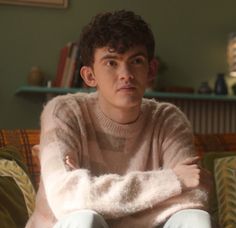 a young man sitting on top of a couch in front of a book shelf with his arms crossed