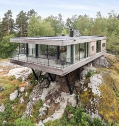 a house built on top of a cliff in the middle of trees and rocks with glass walls