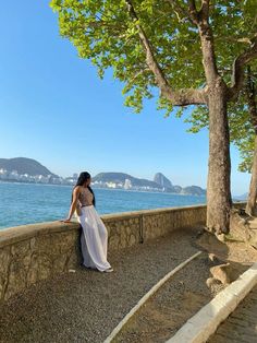 a woman in a white dress standing on the edge of a stone wall next to water