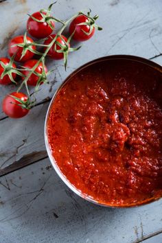 a bowl of tomato sauce next to some tomatoes