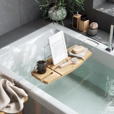 a bath tub with a wooden tray on the edge holding a book, cup and other items