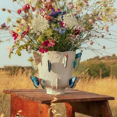 a vase filled with lots of flowers sitting on top of a wooden table next to a field