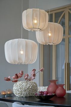 three white lanterns hanging from the ceiling above a table with flowers and candles on it