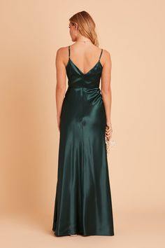 a woman wearing a green satin gown with spaghetti straps and open back, looking down at the