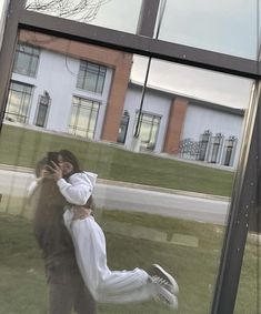 a man and woman are kissing in front of a building with large windows on the grass