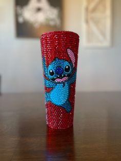 a red and blue cup sitting on top of a wooden table covered in sequins