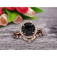 a black diamond ring sitting on top of a wooden table next to pink tulips