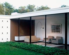 a living room with glass walls and furniture in the middle of green grass covered yard