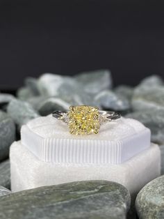 a fancy yellow diamond ring sitting on some rocks