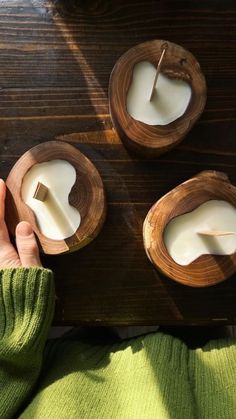 a person sitting at a table with three small wooden bowls filled with white candle holders