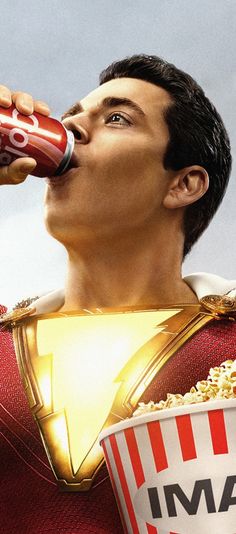 a man in a superman costume drinking from a red and white cup with popcorn on it