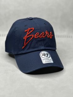 This is a navy CHI Bears script 47 clean up adjustable hat that is hand embellished with varying sizes of genuine transparent orange Swarovski crystals on the front text. This hat features over 150+ varying size Swarovski crystals. - 100% Cotton - Matching fabric strap & buckle - One Size Fits All - Raised Embroidered Logo - 150+ Swarovski orange crystals individually placed by hand - Ready to ship in 1 week from San Diego, CA Adjustable Rhinestone Baseball Cap With Curved Brim, Navy Curved Brim Hat For Game Day, Casual Cap With Rhinestones, Casual Rhinestone Cap, Navy Adjustable Baseball Cap For Fans, Adjustable Curved Brim Baseball Cap For Game Day, Adjustable Curved Brim Hats For Fan Gear, Adjustable Curved Brim Fan Gear Hats, Casual Rhinestone Snapback Hat