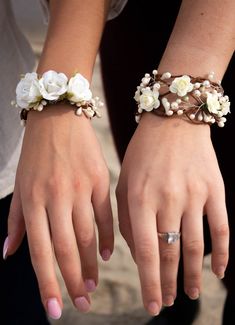 two women wearing bracelets with white flowers on them and one woman's hand