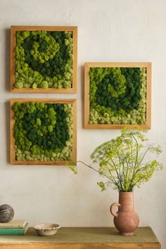 three square wooden frames with green plants in them on a table next to a vase