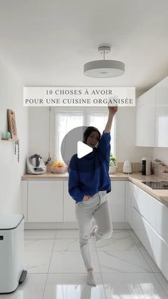 a woman standing in a kitchen holding up a sign that reads 10 choses a avoir pour une cuisine organicise