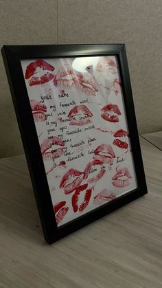 a black frame with red lipstick drawn on it in front of a white wall and wooden floor