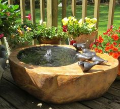 an outdoor fountain with flowers and potted plants in the background on a wooden deck